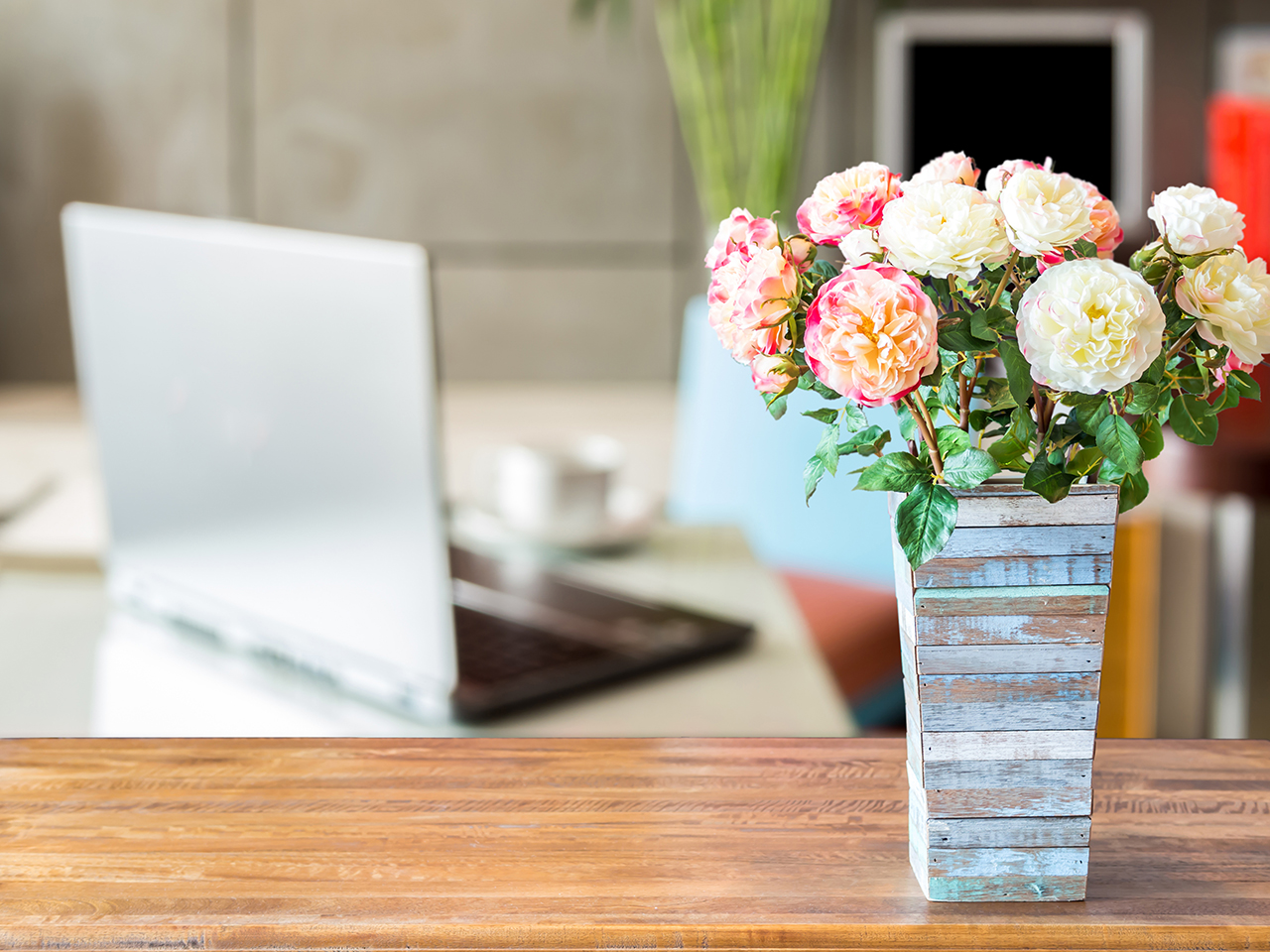 Artificial flower vase over blurred image of modern workspace background