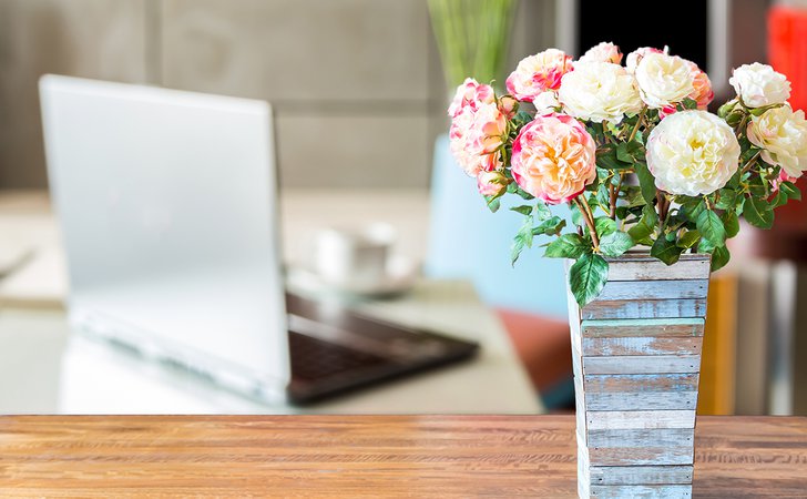 Artificial flower vase over blurred image of modern workspace background